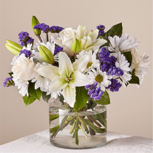 Beyond Blue Bouquet with white lilies, daisies, and purple flowers in a clear vase.