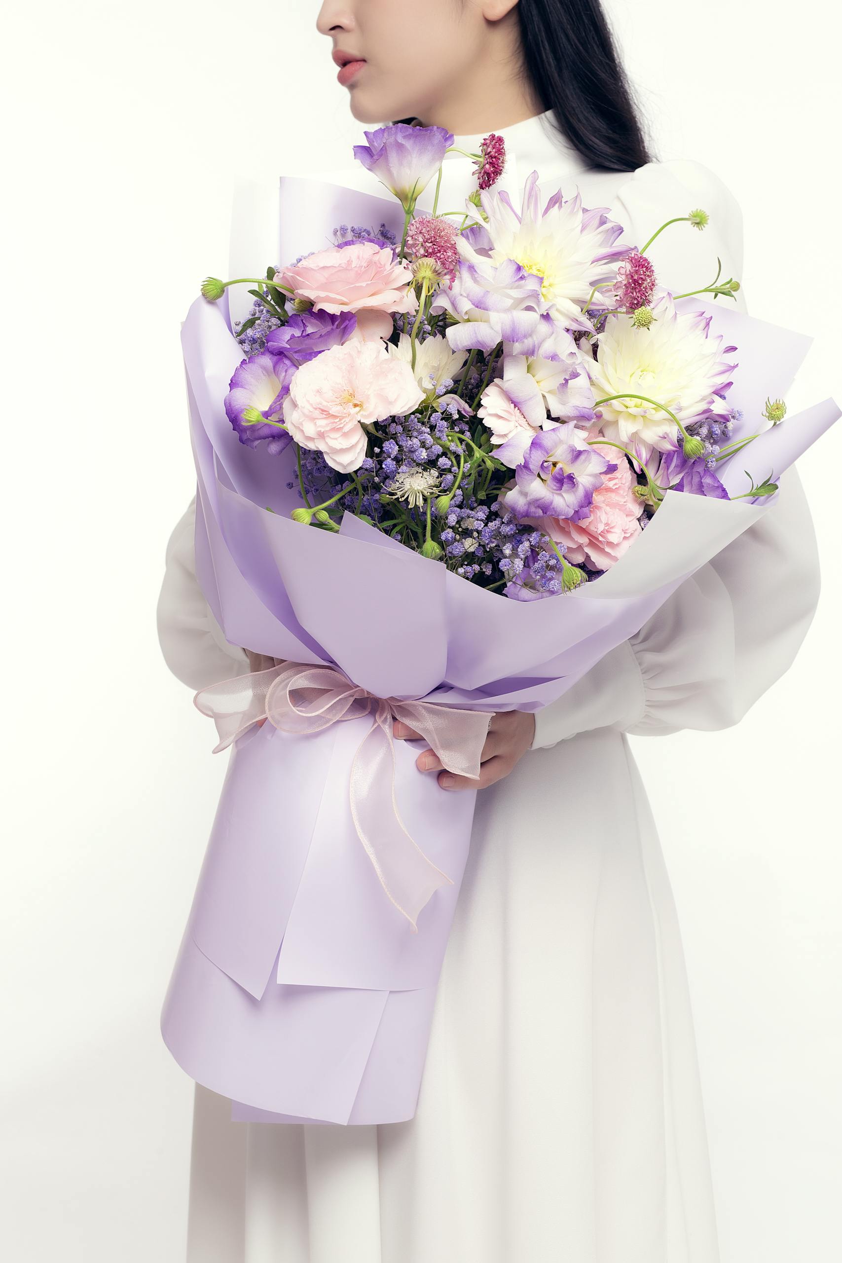 A woman in a white dress holding a beautiful pastel flower bouquet, exuding elegance and simplicity.