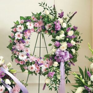 Pink, purple, and white floral wreath on a stand with a purple bow.