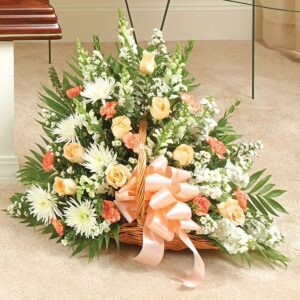 Peach and white flowers in a wicker basket with a large peach bow.