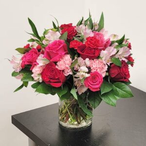 A bouquet of red and pink roses with carnations and alstroemeria, arranged in a clear glass vase.