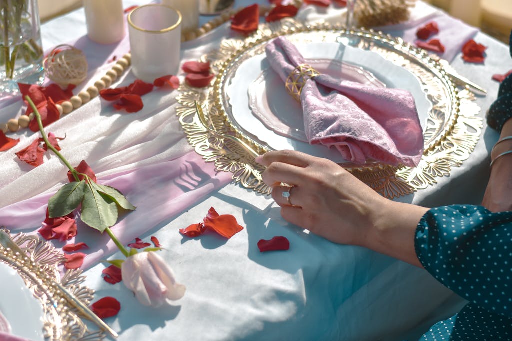 An elegant table setting with rose petals, fine china, and a decorative napkin for a special occasion.