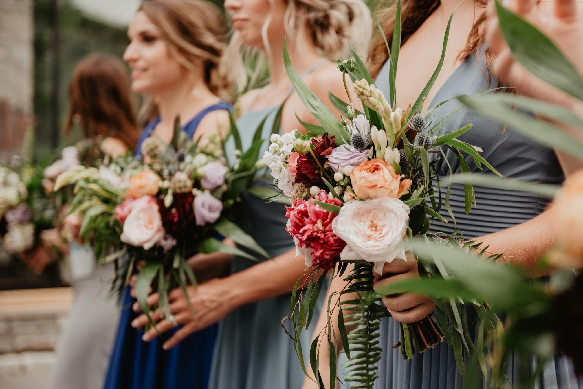 Bridesmaids in blue dresses holding vibrant bouquets during a wedding ceremony.