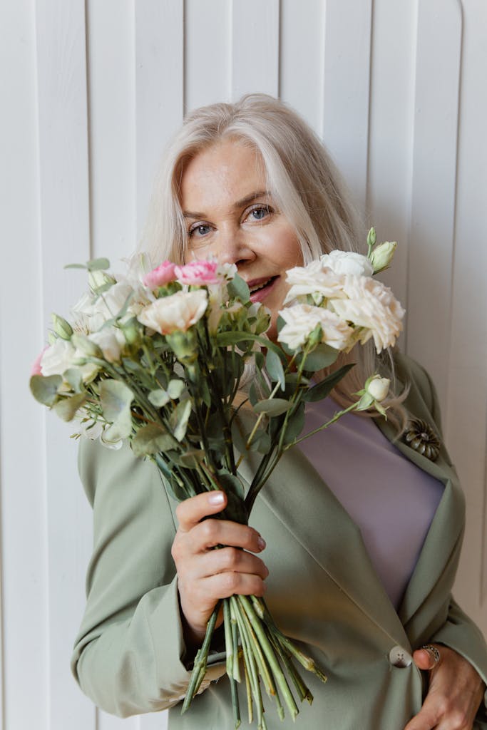Charming senior woman with blond hair holding a fresh flower bouquet against a white backdrop.