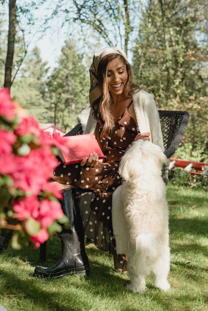 Happy woman in a polka dot dress outdoors, smiling and petting her fluffy dog.