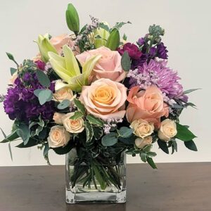 A beautiful bouquet of roses, lilies, and purple flowers arranged in a clear glass vase.