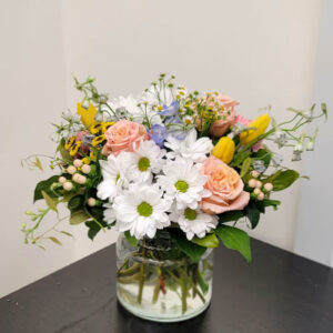 A vibrant bouquet of white daisies, pink roses, yellow tulips, and mixed greenery.