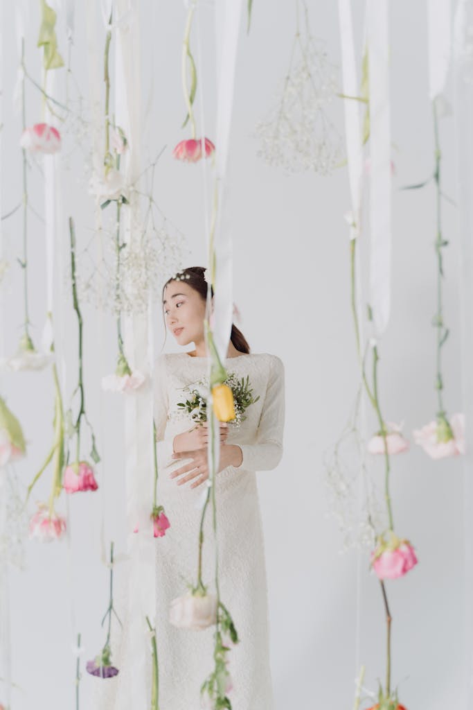 Woman arranging oversized artificial flowers on wall in elegant indoor setting.