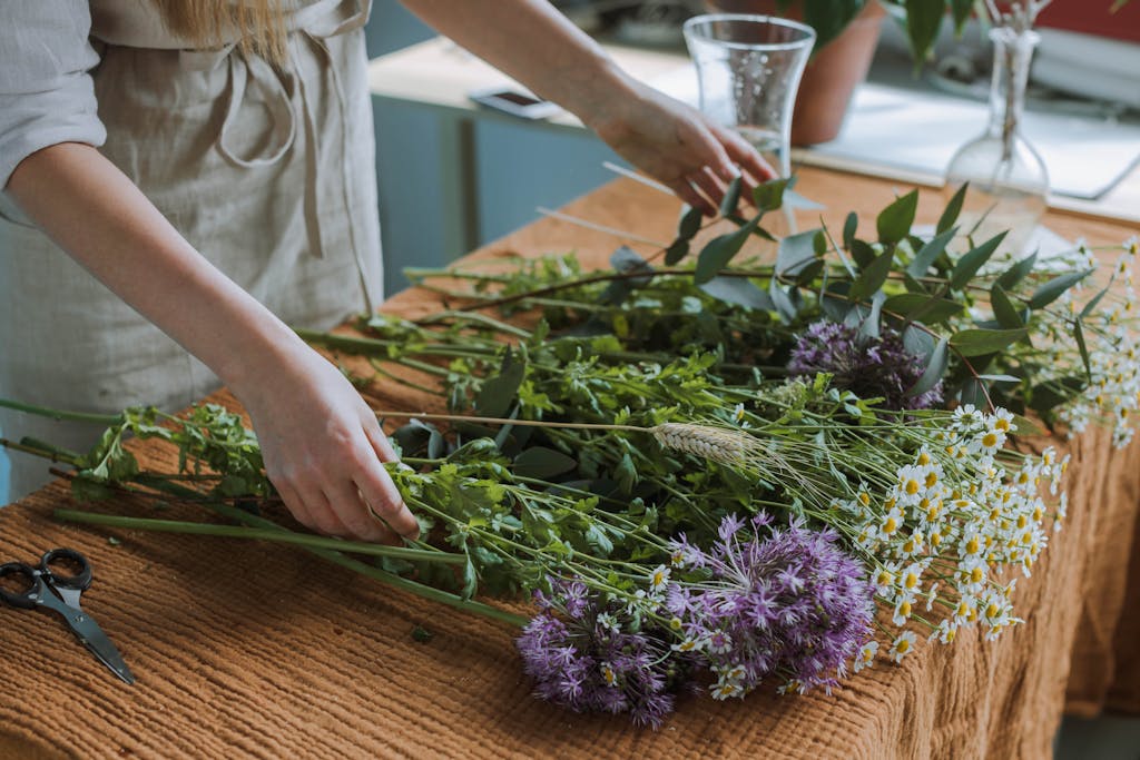 A woman arranges a bouquet of daisies and purple flowers on a wooden table.