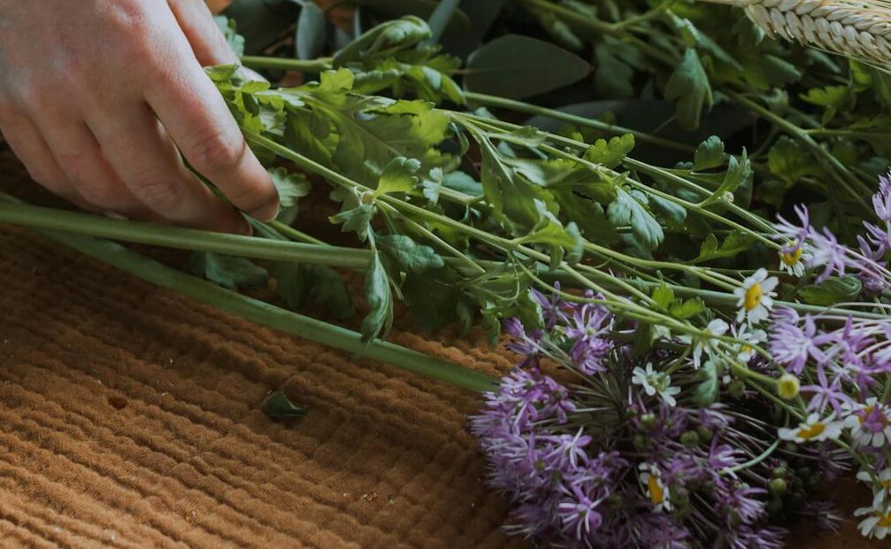 A woman arranges a bouquet of daisies and purple flowers on a wooden table.